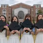 Women college students holding their graduation day caps in front of their college